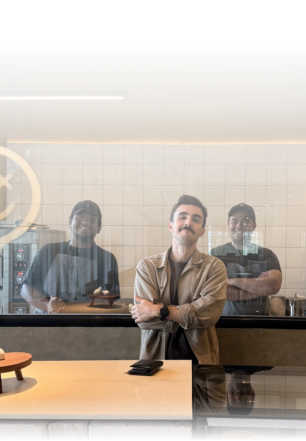 Gonzalo at the Loca Cheesecakes store with his two bakers smiling behind the kitchen window